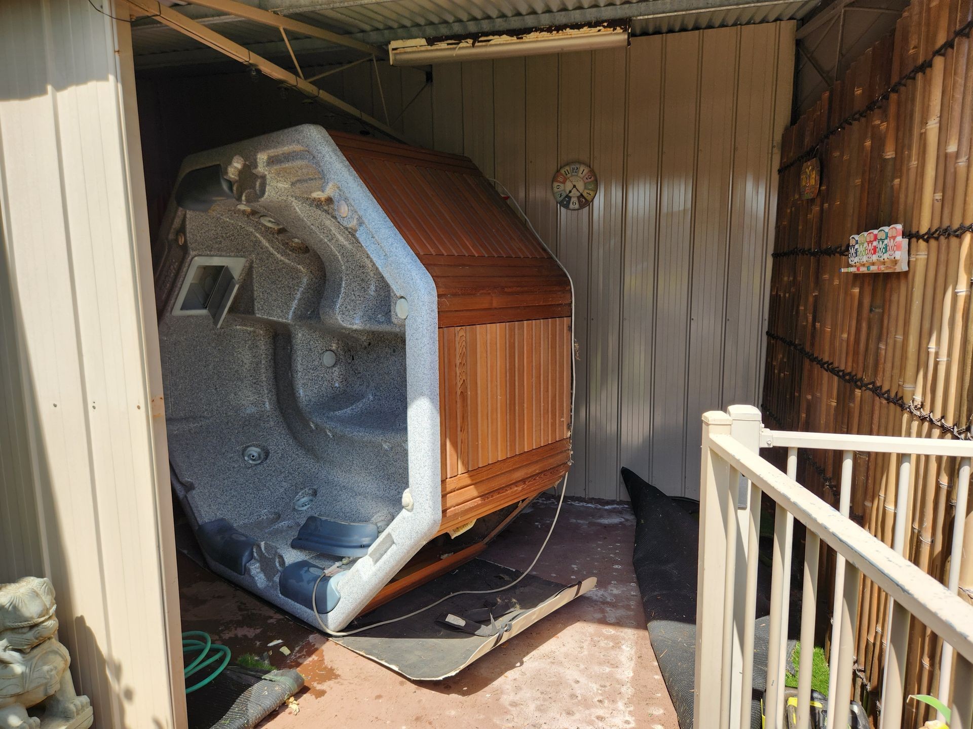 Hot tub flipped on its side inside a shed with bamboo walls and garden hose.